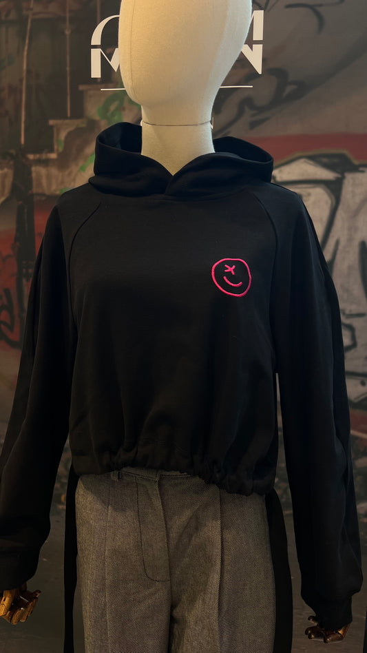 Auf einer Schneider-Puppe ist der geraffte Hoodie mit pinkem gestickten Smiley zu sehen.