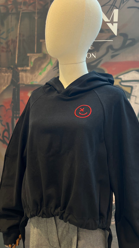 Auf einer Schneider-Puppe ist der geraffte Hoodie mit rotem gestickten Smiley zu sehen.